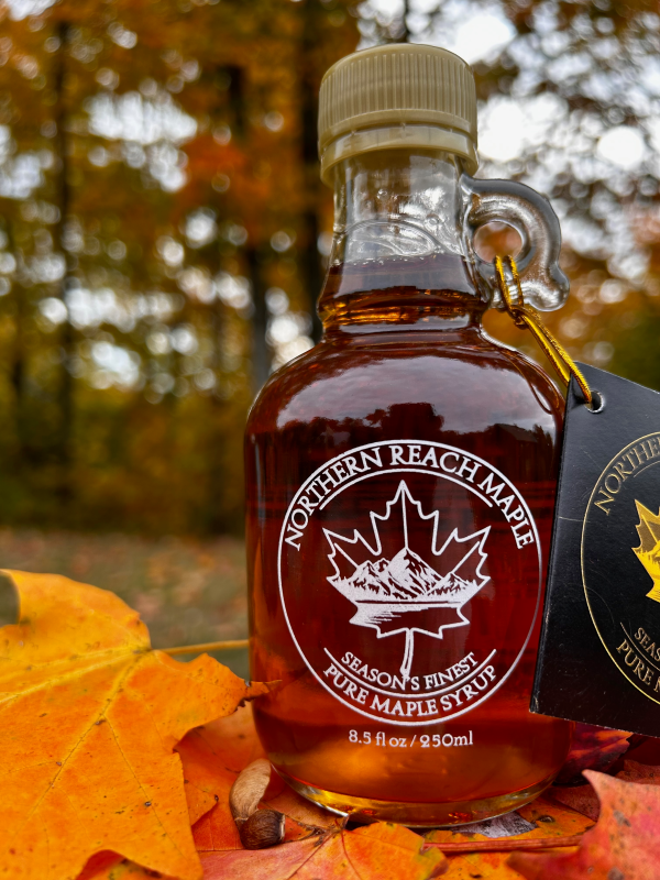 A bottle of Season's Finest, capturing the best of our maple syrup season in front of autumn leaves in Northern Maine.