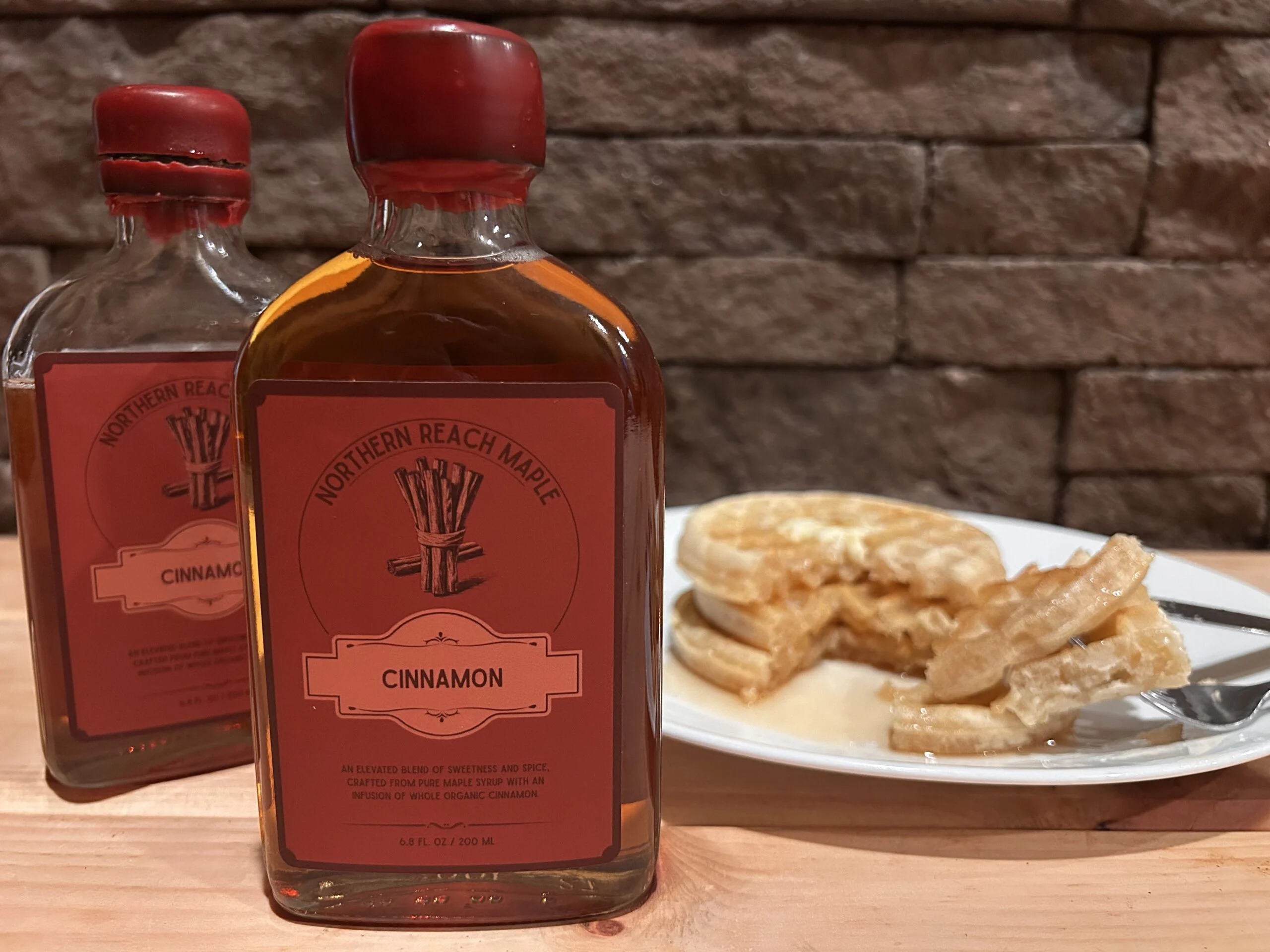 Bottles of cinnamon infused maple syrup shown in front of waffles
