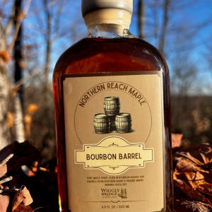 A bottle of Northern Reach Maple's bourbon barrel aged maple syrup with fall leaves in the background.