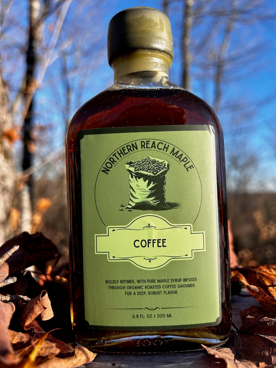 A bottle of Northern Reach Maple's coffee infused maple syrup with fall leaves in the background.