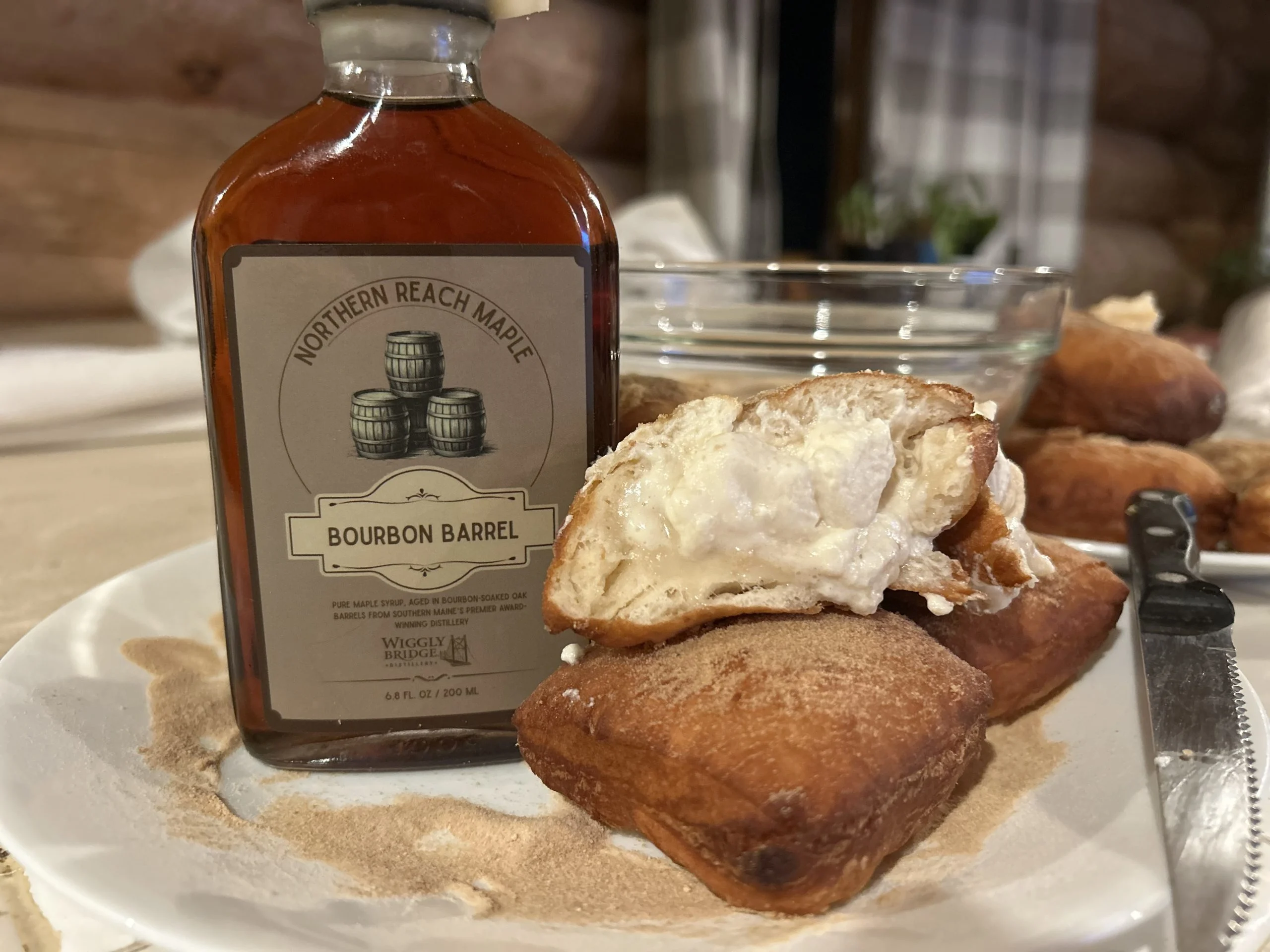 A bottle of bourbon barrel aged maple syrup along side a filled beignet pastry.
