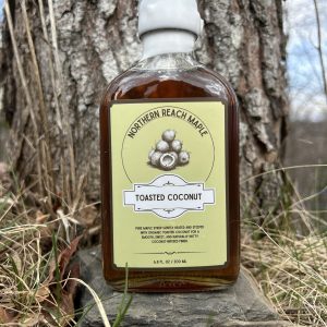 A bottle of Northern Reach Maple Toasted Coconut Maple Syrup outside in front of a maple tree