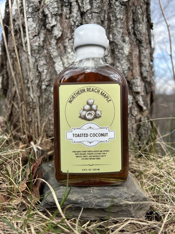 A bottle of Northern Reach Maple Toasted Coconut Maple Syrup outside in front of a maple tree