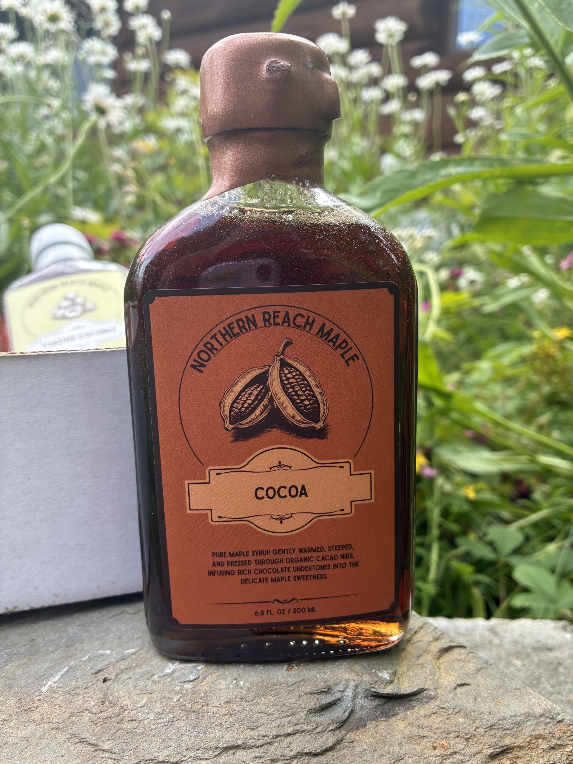 Cocoa infused maple syrup in front of the Berry, Cacao, and Copra Flavor Trio box.