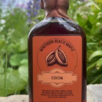 A bottle of Northern Reach Maple Cocoa Infused Maple Syrup in front of some Northern Maine Lupins.