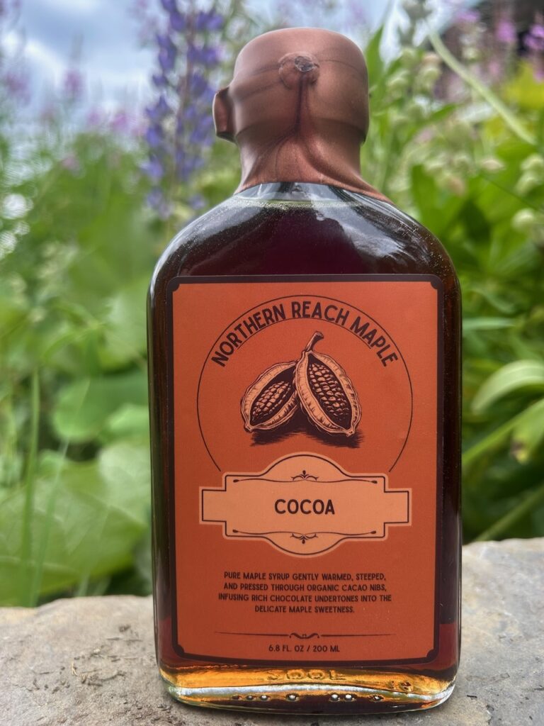 A bottle of Northern Reach Maple Cocoa Infused Maple Syrup in front of some Northern Maine Lupins.