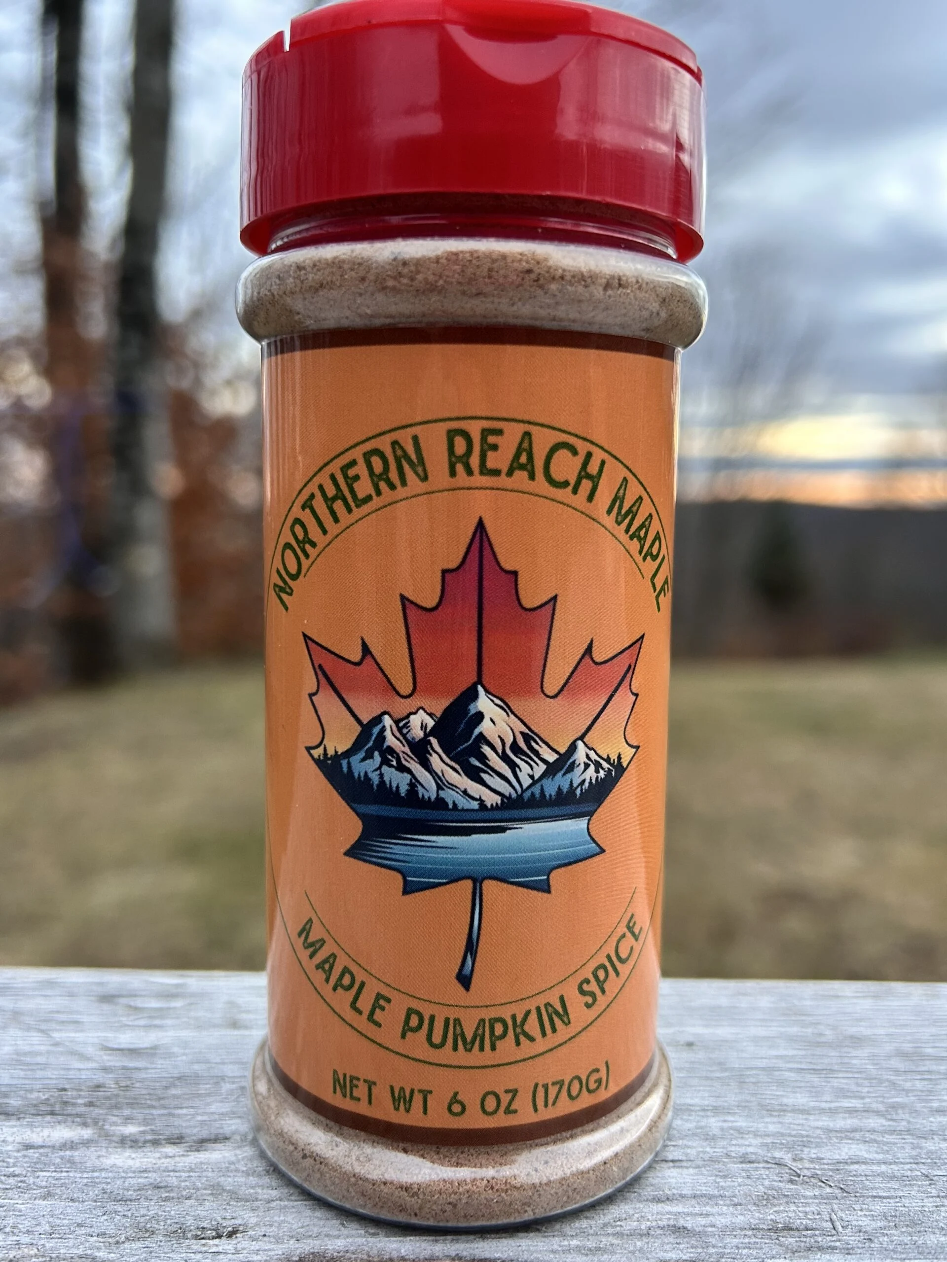 A 6oz Maple Pumpkin Spice shaker on top of a picnic table with sunset in the background.
